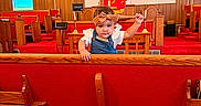 Rosalie joined the competition — help win amazing prizes! baby, candlesticks, child, church, cross, curious, decor, headband, indoor, lighting, overalls, person, pew, playful, red_carpet, red_upholstery, television, toddler, white_shirt, wooden_furniture