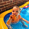 Rosalie joined the competition — help win amazing prizes! baby, child, pool, water, toy, orange, blue, brick_wall, inflatable, sitting, wet, chewing, curious, play, summer, fun, cute, indoors, plastic, colorful