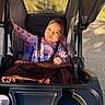 baby, stroller, blanket, bottle, onesie, child, outdoor, sunlight, shadow, face, blue_eyes, hand, plastic, seat, toy, comfort, infant, clothing, cute, portrait