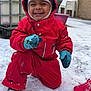child, toddler, snow, red_snowsuit, mittens, outdoor, winter, smiling, happy, play, snow_covered, footwear, hat, crouching, plastic_chairs, building, window, rustic, daylight, cold_weather