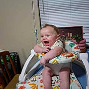 Tatum Jordan is registered to the contest to win money with this photo: baby, high_chair, smiling, indoor, plant, furniture, child, person, table, chair, window_blinds, picture_frame, colorful, happy, legs, feet, clothing, toy_ring, face, arm