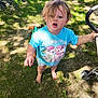 child, toddler, barefoot, blue_shirt, my_little_pony, grass, stroller, outdoor, sunlight, fence, curly_hair, open_mouth, holding, summer, nature, young_child, casual, daylight, playtime, backyard