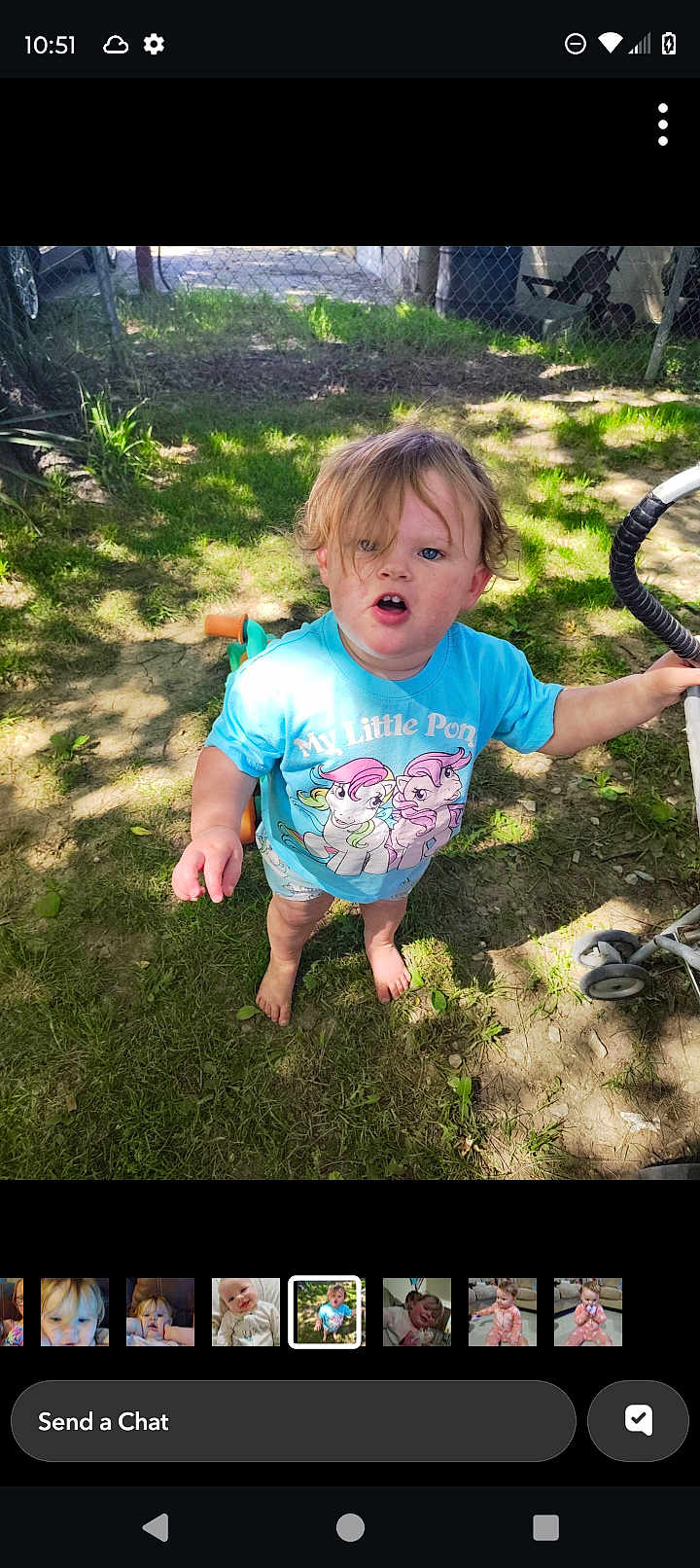Ava Grace is registered to the contest to win money with this photo: child, toddler, barefoot, blue_shirt, my_little_pony, grass, stroller, outdoor, sunlight, fence, curly_hair, open_mouth, holding, summer, nature, young_child, casual, daylight, playtime, backyard