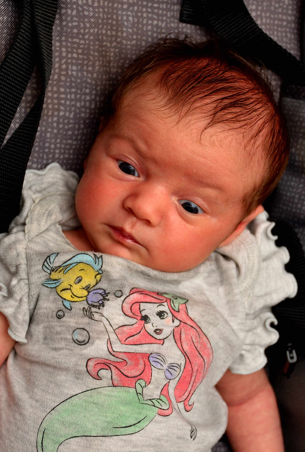 Gianna joined the competition — help win amazing prizes! baby, infant, child, face, expression, clothing, tshirt, cartoon, disney, ariel, flounder, portrait, closeup, person, cute, young, skin, hair, sitting, indoors