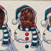 Starr is registered to the contest to win money with this photo: child, portrait, smiling, snowman, costume, winter, scarf, hat, beads, braids, colorful, festive, christmas, wall, artwork, pattern, close_up, face, indoors, playful