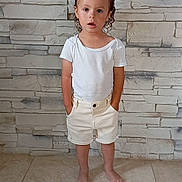Lino participe au concours pour gagner de l'argent avec cette photo : bare_legs, barefoot, casual_clothing, child, curious, curly_hair, floor_tiles, hands_in_pockets, indoor, light_skin, neutral_expression, portrait, short_sleeves, shorts, standing, stone_wall, textured_wall, tile_floor, white_tshirt, young_kid