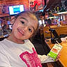 Eliannie is registered to the contest to win money with this photo: casual, child, cozy, happy, indoor, juice_box, lighting, mounted_animal_head, person, pink_butterfly, portrait, restaurant, seated, smiling, table, television, white_sweater, wooden_chair, wooden_interior, young_child