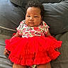 baby, infant, child, portrait, sitting, couch, gray_couch, red_tutu, dress, colorful_clothing, strawberry_pattern, cartoon_pattern, curly_hair, face, eyes, serious_expression, indoor, home, fabric, photography