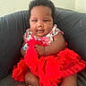 Abrielle is registered to the contest to win money with this photo: baby, infant, child, portrait, sitting, couch, red_dress, tutu, strawberry_pattern, curly_hair, brown_skin, face, eyes, serious_expression, indoor, furniture, home, photography, baby_clothing, close_up