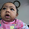 Neriah is registered to the contest to win money with this photo: baby, child, face, bib, drool, hand, indoor, curious, pink, clothing, portrait, young_child, person, looking_up, expression, skin, head, cute, holding, floral_pattern