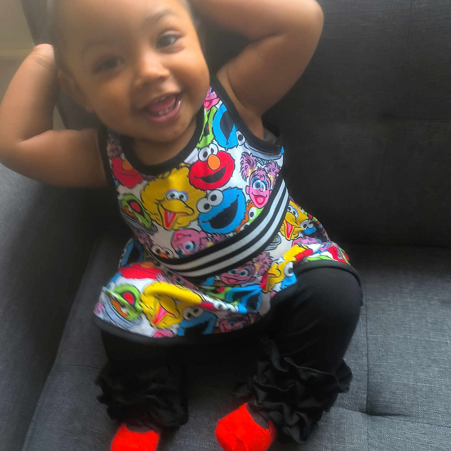 Neriah joined the competition — help win amazing prizes! child, toddler, smiling, colorful_clothing, dress, socks, orange_socks, sesame_street, indoor, chair, cushion, happy, playful, person, portrait, cute, baby, seated, furniture, black_pants