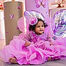 baby, child, pink_dress, butterfly_wings, balloons, party, celebration, smiling, floor, decorations, headpiece, curly_hair, indoor, cute, festive, happy, toddler, colorful, portrait, sparkles