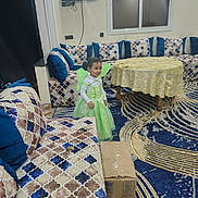 Maryam joined the competition — help win amazing prizes! child, toddler, fairy_costume, green_dress, smiling, indoors, living_room, sofa, cushions, table, tablecloth, television, window, carpet, rug, furniture, portrait, standing, home_decor, cardboard_box