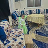cardboard_box, carpet, child, cushions, fairy_costume, furniture, green_dress, home_decor, indoors, living_room, portrait, rug, smiling, sofa, standing, table, tablecloth, television, toddler, window