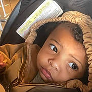 Jeffrey is registered to the contest to win money with this photo: toddler, child, face, hood, jacket, stroller, car_seat, indoor, warning_label, curious, looking_away, baby, clothing, seat, soft_lighting, expression, young_child, person, portrait, casual