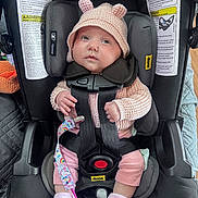 Isabella is registered to the contest to win money with this photo: baby, car_seat, infant, pink_hat, knitted_clothing, pacifier, socks, straps, seatbelt, child, cute, indoors, warning_labels, safety, newborn, clothing, person, car_travel, baby_accessory, soft_toys