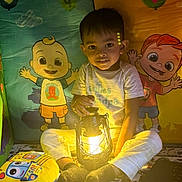 Jayden joined the competition — help win amazing prizes! child, lantern, light, indoor, cartoon, illustration, playmat, toy, socks, pants, tshirt, smile, face, kid, colorful, background, playroom, cozy, warm_light, sitting