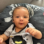 Warren participe au concours pour gagner de l'argent avec cette photo : baby, infant, child, batman, onesie, clothing, pillow, face, portrait, cute, smiling, hand, lying_down, indoors, young_child, expression, soft_light, black, gray, yellow