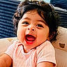 Nyra joined the competition — help win amazing prizes! baby, child, smiling, laughing, curly_hair, pink_clothing, face, person, happy, indoors, cushion, teddy_bear_print, cute, infant, portrait, skin, mouth_open, joy, seat, young