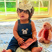 Nyra is registered to the contest to win money with this photo: baby, bedspread, blue, bow, card, child, curly_hair, cute, denim_overalls, headband, indoor, mickey_mouse, natural_light, pink, plush_toy, sitting, stuffed_animal, text, toddler, window