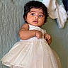 Nyra is registered to the contest to win money with this photo: baby, child, dress, white_dress, pearl, cute, infant, portrait, lying_down, curious, face, skin, hair, indoors, soft_light, texture, hands, expression, closeup, apparel