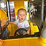 adult, amusement, arcade, background, blue_eyes, child, curious, expression, fun, game, indoor, person, ride, seat, short_hair, steering_wheel, toddler, toy, white_shirt, yellow