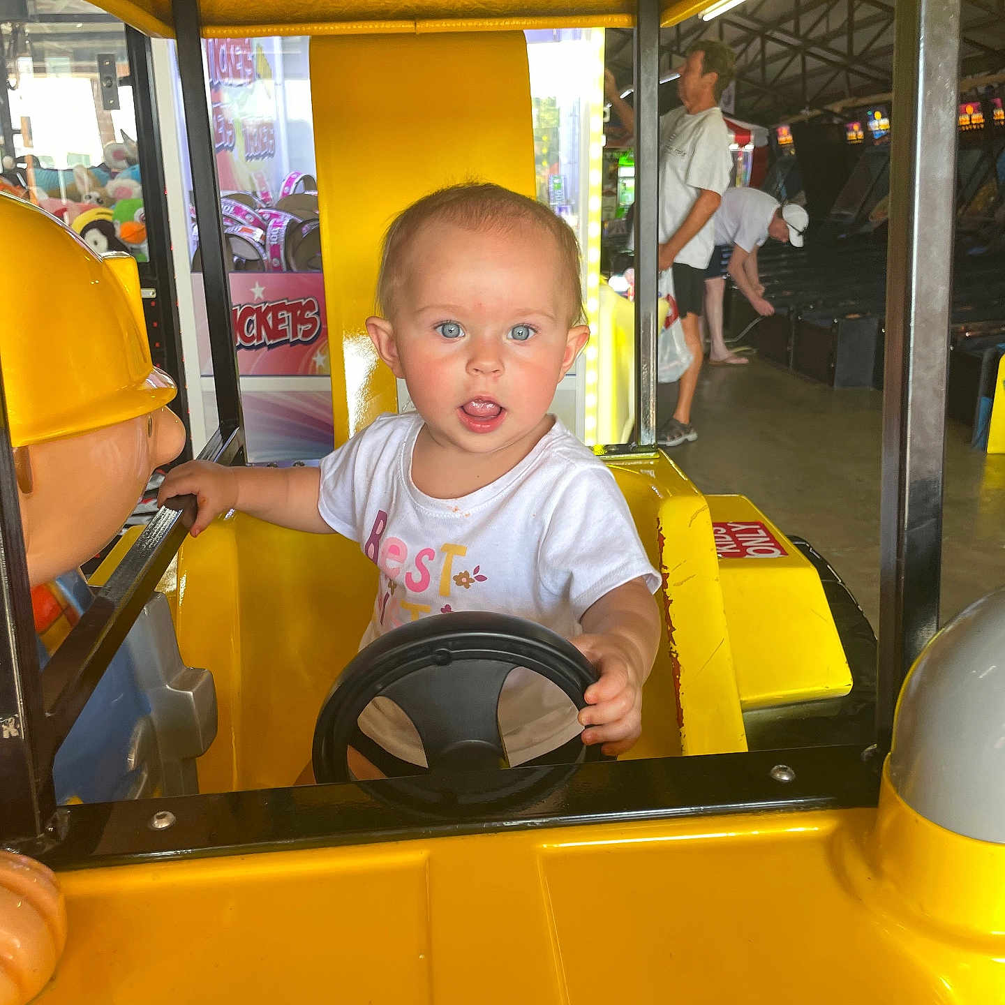 Indikeja joined the competition — help win amazing prizes! adult, amusement, arcade, background, blue_eyes, child, curious, expression, fun, game, indoor, person, ride, seat, short_hair, steering_wheel, toddler, toy, white_shirt, yellow