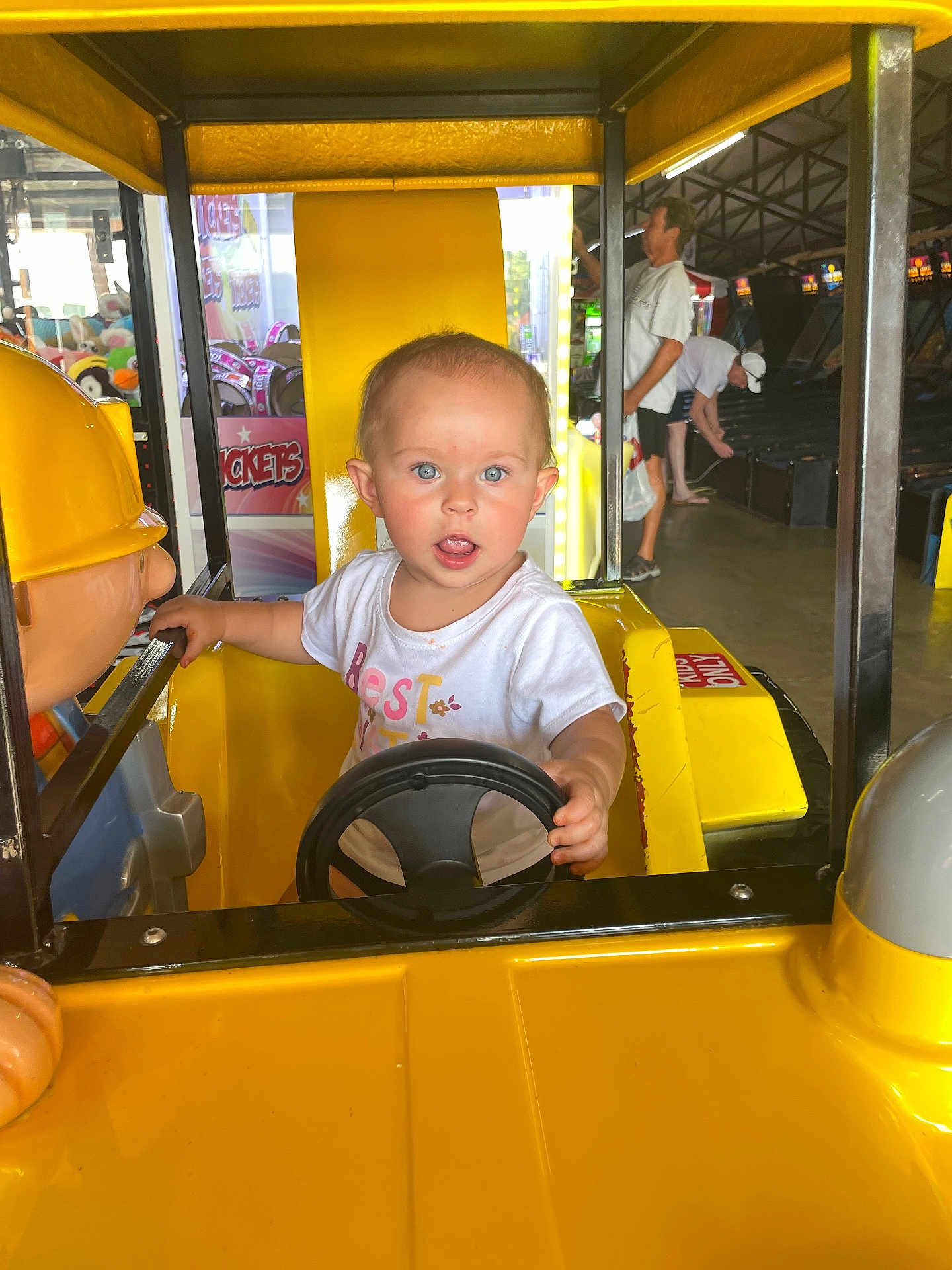 Indikeja joined the competition — help win amazing prizes! adult, amusement, arcade, background, blue_eyes, child, curious, expression, fun, game, indoor, person, ride, seat, short_hair, steering_wheel, toddler, toy, white_shirt, yellow