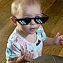 Indikeja is registered to the contest to win money with this photo: baby, casual_wear, child, colorful_clothing, cute, expression, eyewear, face, gesture, head, indoor, person, pixelated_glasses, portrait, short_hair, standing, sunglasses, toddler, wooden_floor, young_child