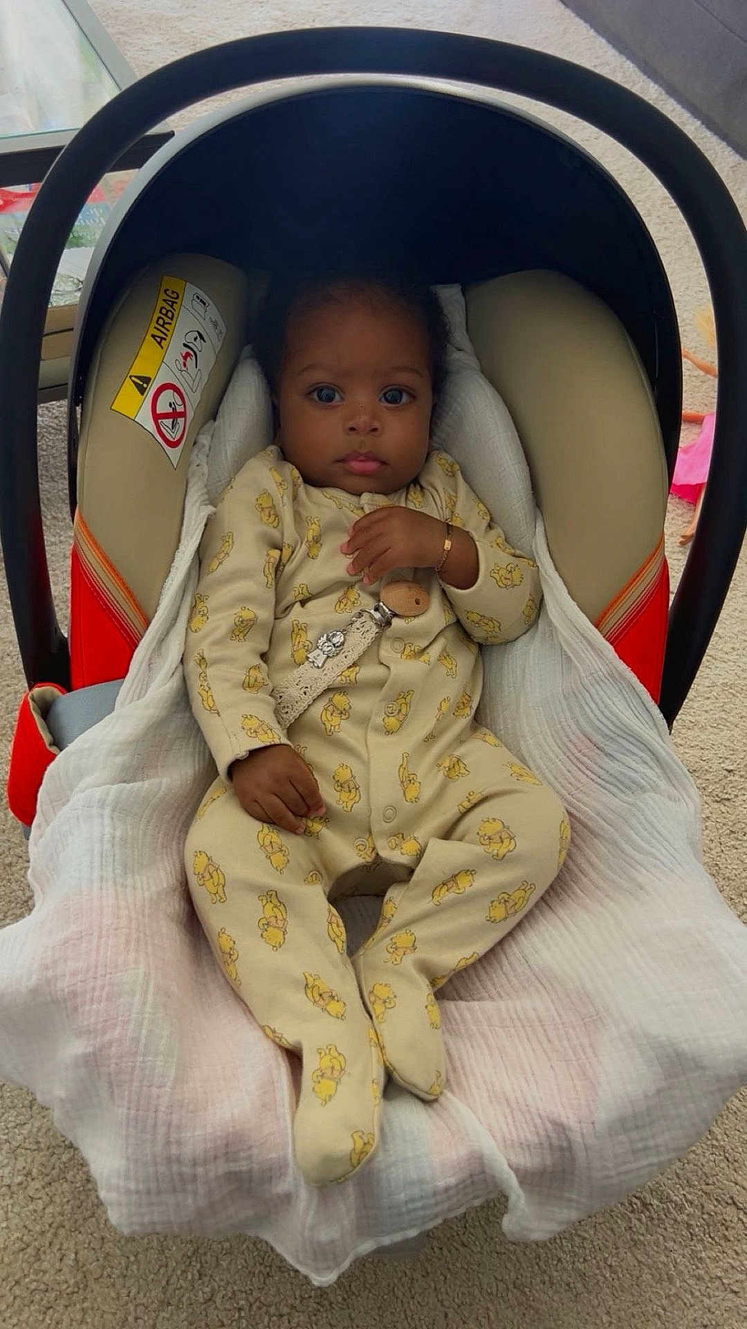 Chayden a rejoint le concours — aidez-le/la à gagner de superbes lots ! baby, child, car_seat, blanket, onesie, yellow_clothing, indoor, carrying_handle, infant, cute, face, person, portrait, seated, carpet, bracelet, pacifier_clip, expression, looking, soft