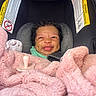 baby, infant, car_seat, blanket, pink, pacifier, smiling, face, curly_hair, child, seatbelt, safety, cozy, indoors, cute, person, young_child, car_accessory, expression, wrapped