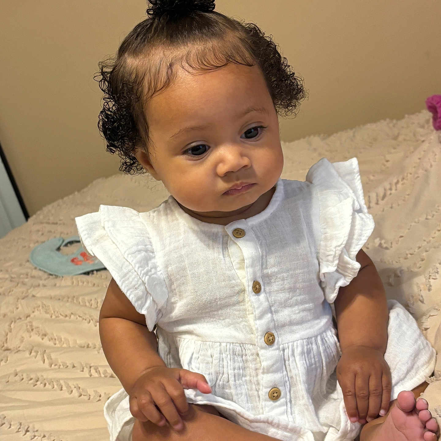 Ayvia joined the competition — help win amazing prizes! baby, bed, bedspread, buttoned_clothing, calm, child, curious, curly_hair, cute, face, feet, hair_bun, hands, indoor, infant, portrait, sitting, skin, thoughtful, white_dress