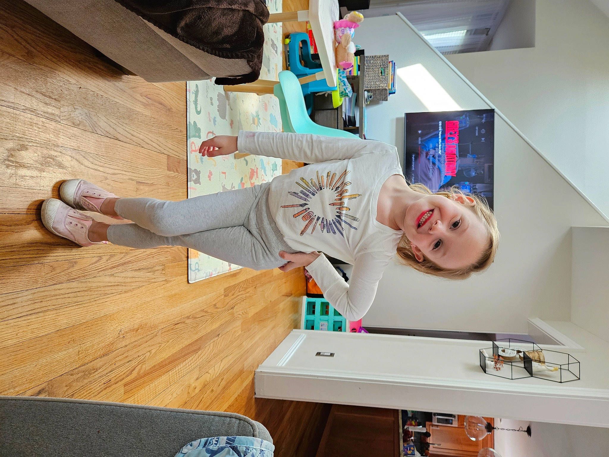 Madelyn is registered to the contest to win money with this photo: baby, building, child, comfort, display_device, flooring, hardwood, home_appliance, house, joy, machine, person, room, shelf, shelving, smile, t_shirt, table, toddler, varnish