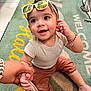 baby, child, sunglasses, smile, hand_holding, sitting, clothing, bracelet, floor_mat, indoor, person, cute, reflection, happy, portrait, infant, casual_wear, accessory, young_child, playful