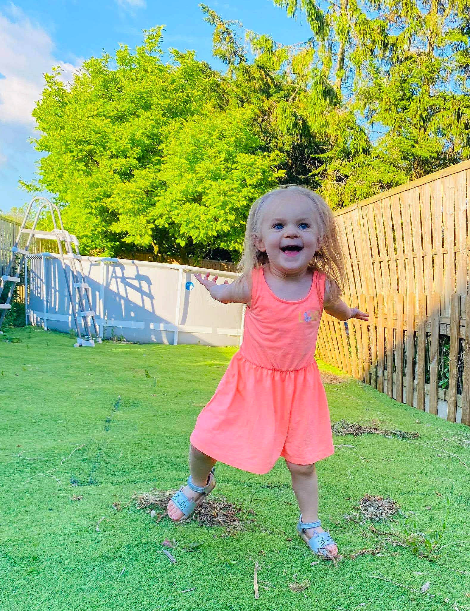 Lïa a rejoint le concours — aidez-le/la à gagner de superbes lots ! baby_toddler_clothing, blue, botany, dress, eye, facial_expression, fun, grass, grassland, happy, joy, leaf, leisure, people_in_nature, person, plant, sky, smile, sunlight, toddler