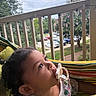 child, toddler, pacifier, hammock, outdoor, porch, railing, trees, cars, sky, cloudy, curious, colorful, clothing, person, young_child, nature, daytime, relaxing, baby