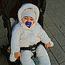 baby, child, stroller, pacifier, winter_clothing, white_jacket, knit_hat, outdoor, pavement, bundle_up, cold_weather, infant, seated, cute, cozy, baby_gloves, baby_booties, urban, sidewalk, peaceful