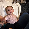 baby, blanket, couch, striped_bag, patterned_shirt, black_pants, indoor, person, child, seated, cozy, furniture, legs, comfort, curious, young_child, soft_lighting, home_interior, relaxed, textile