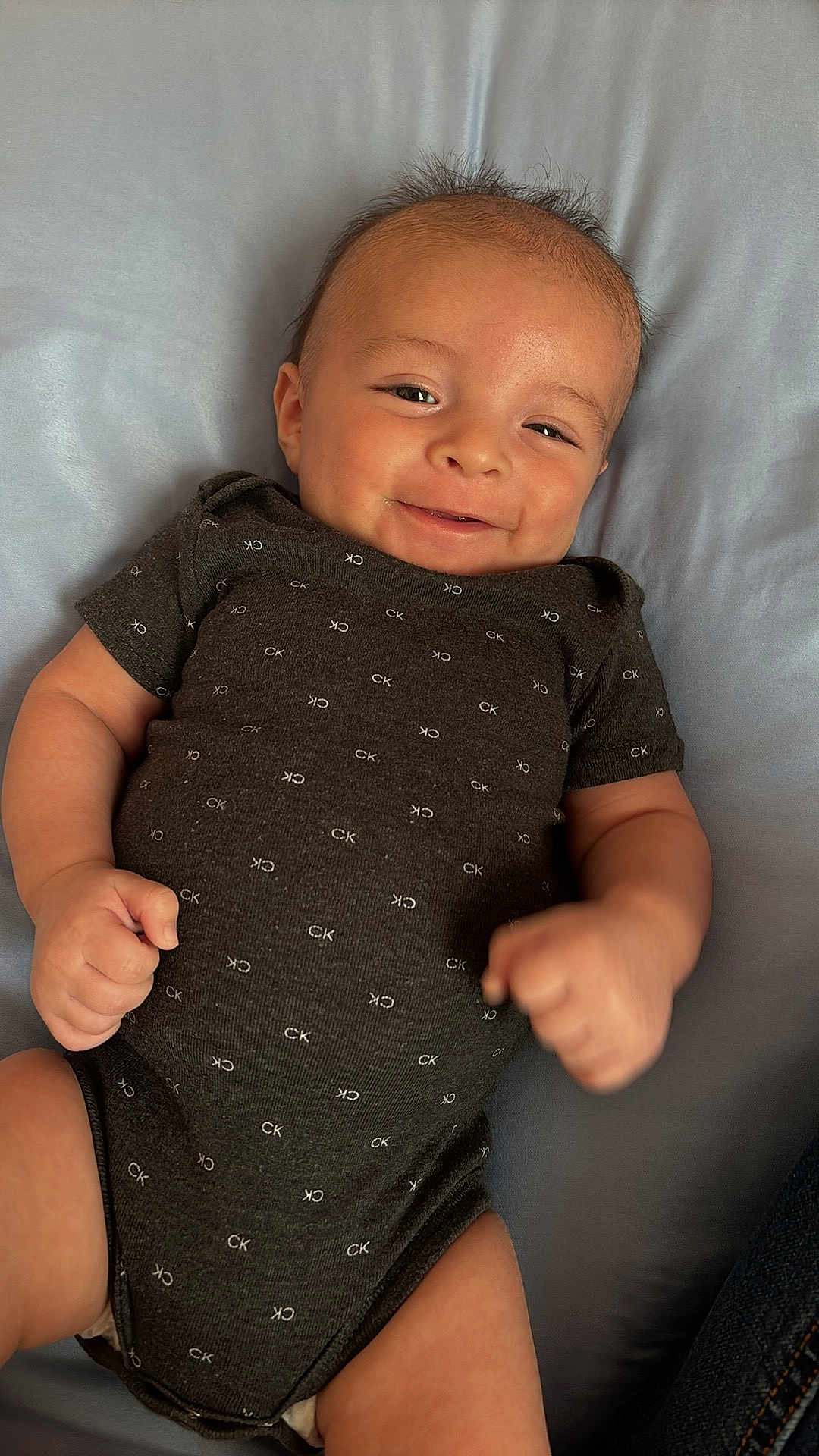 Emilio Ray joined the competition — help win amazing prizes! baby, infant, smile, onesie, clothing, happy, fist, lying_down, skin, head, face, cheeks, short_sleeves, pattern, fabric, child, young, cute, indoors, soft_surface
