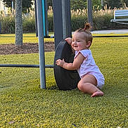Remi is registered to the contest to win money with this photo: baby, child, grass, outdoor, park, playground, tire, bench, trees, smiling, person, greenery, sunlight, playing, cute, happy, nature, grass_field, daytime, casual_clothing