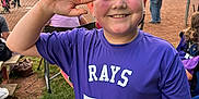 Davis is registered to the contest to win money with this photo: baseball_field, boy, chain_link_fence, child, fun, game, grass, happy, hat, number_77, outdoor, people, purple_shirt, recreation, smiling, spectators, sports_jersey, sunset, team, water_bottle