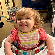 Layla joined the competition — help win amazing prizes! baby_walker, bib, carpet, child, curly_hair, cute, face, furniture, hand, happy, home, indoor, living_room, person, pink_shirt, playtime, smile, television, toddler, toy