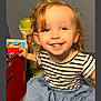 blue_eyes, blue_skirt, carpet, casual_clothing, child, curly_hair, earrings, floor, happy, indoor, person, playful, portrait, room, smiling, striped_shirt, toddler, toy_chest, toys, young_child