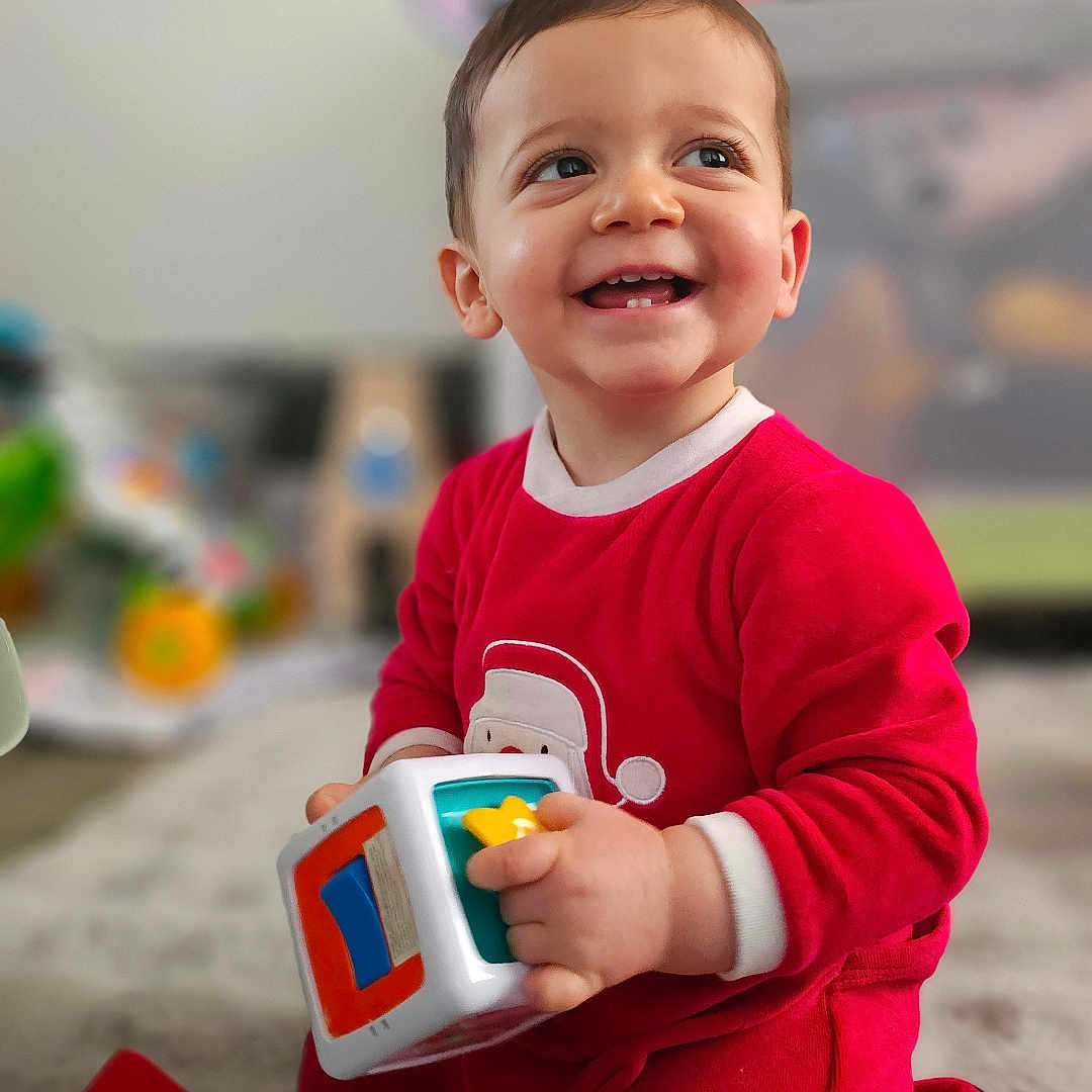 Andrea a rejoint le concours — aidez-le/la à gagner de superbes lots ! toddler, child, smiling, red_onesie, toy, indoor, carpet, playing, happy, baby, cute, kneeling, young_child, colorful_toy, face, person, home, floor, expression, clothing