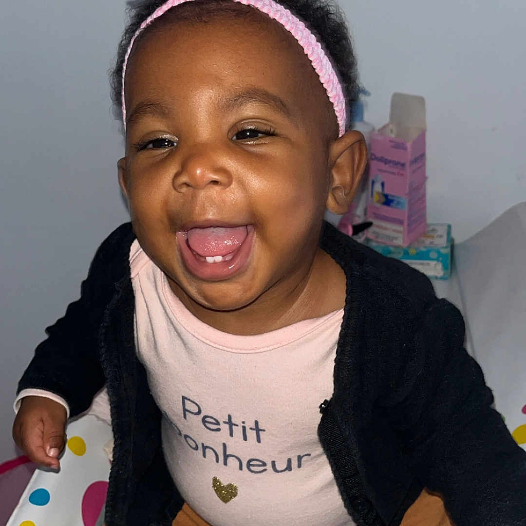 Kélynda participe au concours pour gagner de l'argent avec cette photo : baby, black_jacket, brown_pants, child, closeup, clothing, cute, expression, face, happy, headband, indoor, infant, joyful, person, pink_bow, playful, sitting, smiling, toddler