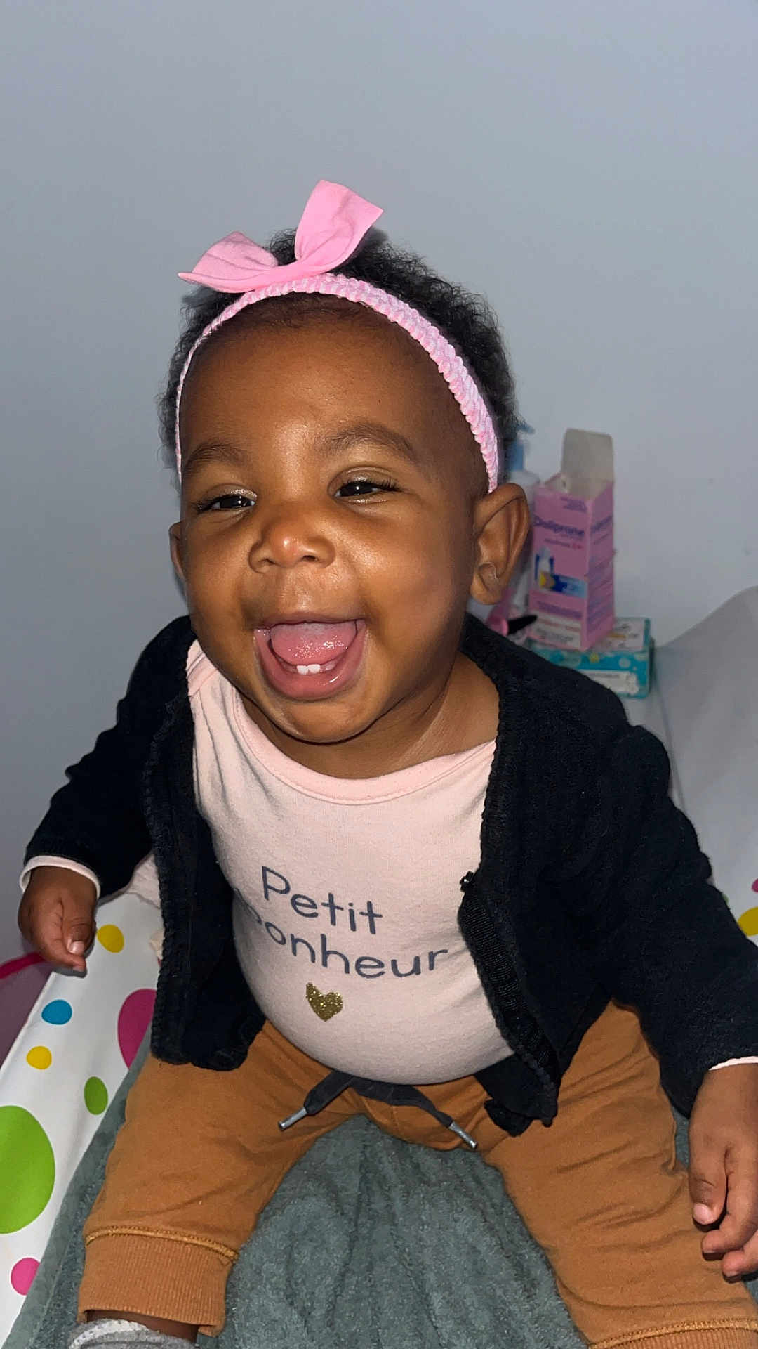 Kélynda participe au concours pour gagner de l'argent avec cette photo : toddler, smiling, pink_bow, headband, baby, happy, child, black_jacket, brown_pants, indoor, person, cute, infant, joyful, sitting, face, closeup, clothing, expression, playful