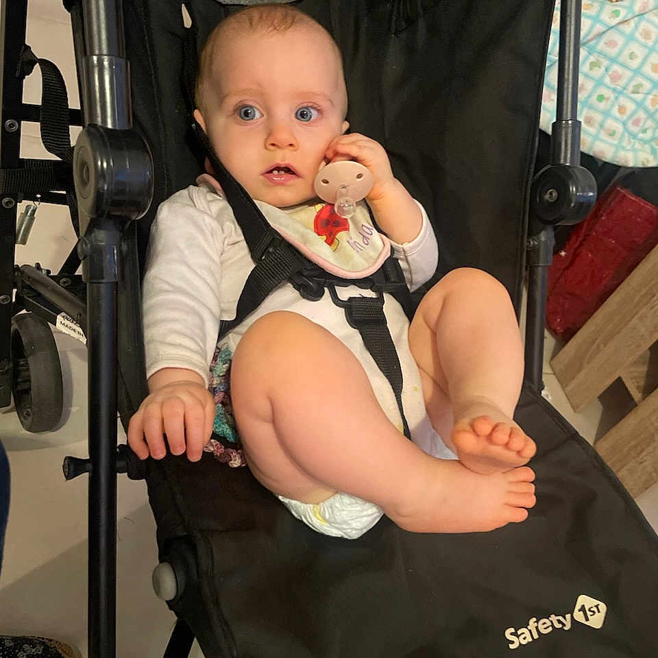 Louve is registered to the contest to win money with this photo: baby, bib, black, blue_eyes, child, clothing, curious, diaper, expression, face, foot, furniture, hand, indoor, infant, pacifier, person, safety_1st, sitting, stroller