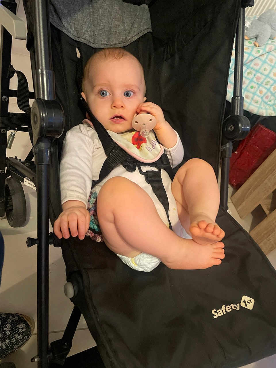 Louve is registered to the contest to win money with this photo: baby, stroller, pacifier, bib, diaper, infant, child, sitting, black, clothing, foot, hand, face, blue_eyes, indoor, safety_1st, expression, curious, person, furniture