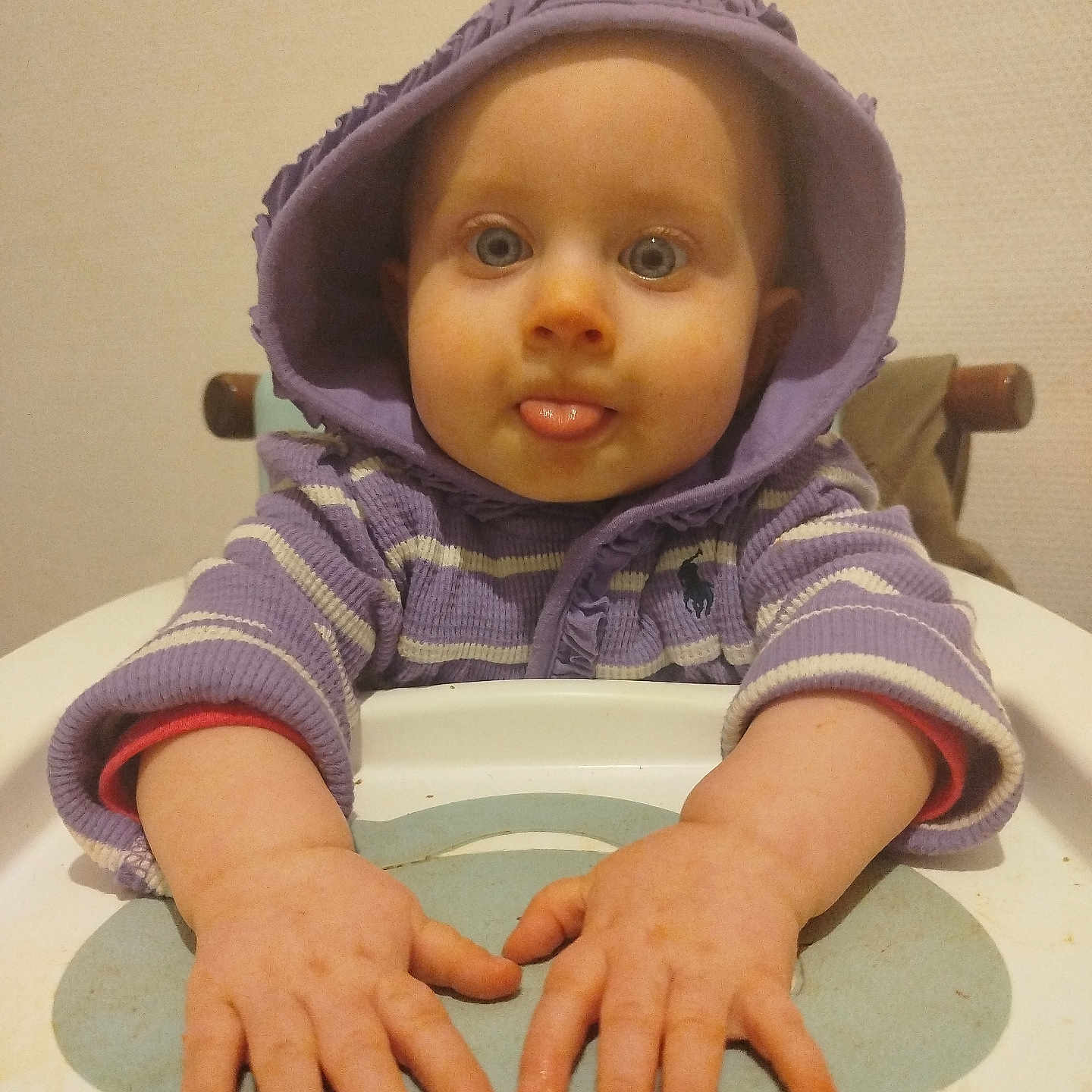 Louve participe au concours pour gagner de l'argent avec cette photo : baby, blue_eyes, child, cute, expression, face, hands, high_chair, hood, indoor, infant, person, playful, portrait, purple_clothing, sitting, sweater, table, tongue_out, young_child