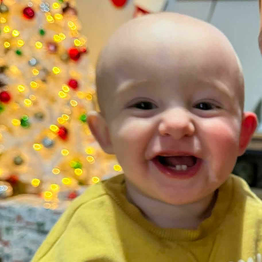 Alyona is registered to the contest to win money with this photo: baby, cheerful, child, christmas_tree, closeup, cute, decorations, face, festive, happy, holiday, home, indoor, infant, joyful, portrait, seasonal, smiling, stockings, yellow_sweater